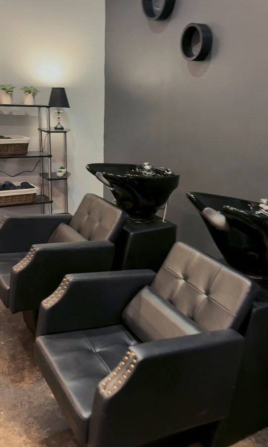 Black leather shampoo chairs and bowls against a gray wall